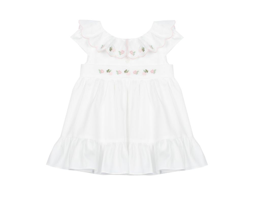 White baby girl dress with pink hand-smocked floral embroidery, scalloped collar, and ruffled hem