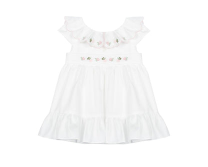 White baby girl dress with pink hand-smocked floral embroidery, scalloped collar, and ruffled hem